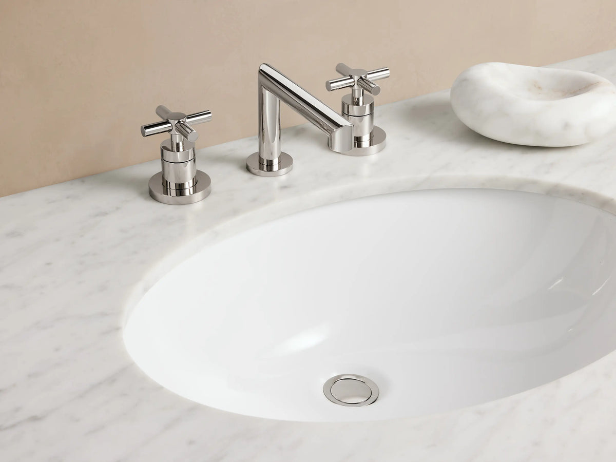 Circular polished nickel drain cover for Lomas Faucet against a white surface, reflecting light subtly.