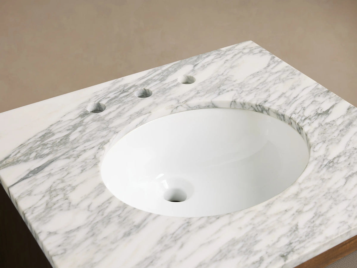 Malone Powder Vanity with white marble countertop, oval sink, dark bronze widespread faucet, soap dispenser & small plant.
