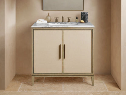 Malone Single Vanity with light wood frame, beige shagreen doors, white marble top, and brass hardware, in a bathroom setting.