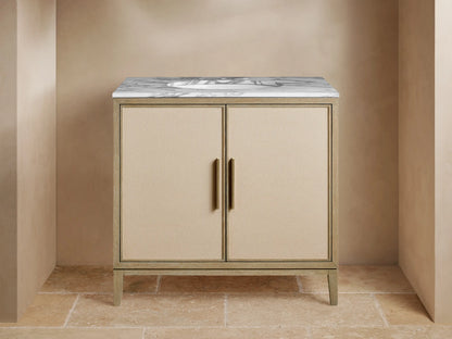Malone Single Vanity with light wood frame, beige shagreen doors, white marble top, and brass hardware, in a bathroom setting.