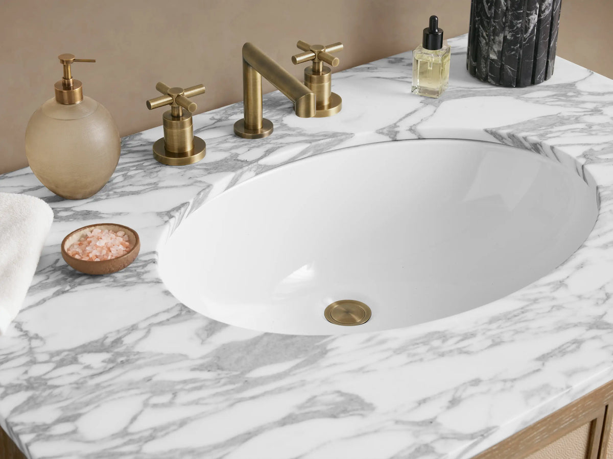Malone Single Vanity with a light bone oak frame, beige textured shagreen doors with brass pulls, and a white marble countertop.