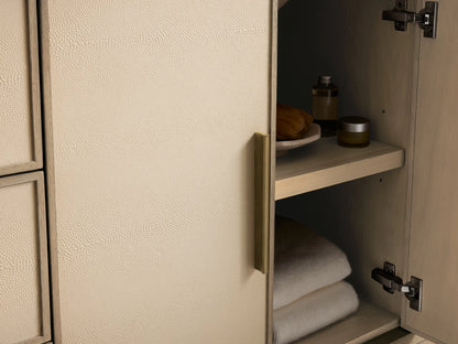Malone Wide Single Vanity, Bone finish. Cream shagreen panels, brass handles. Open drawer reveals white towel & bottles. Marble top.