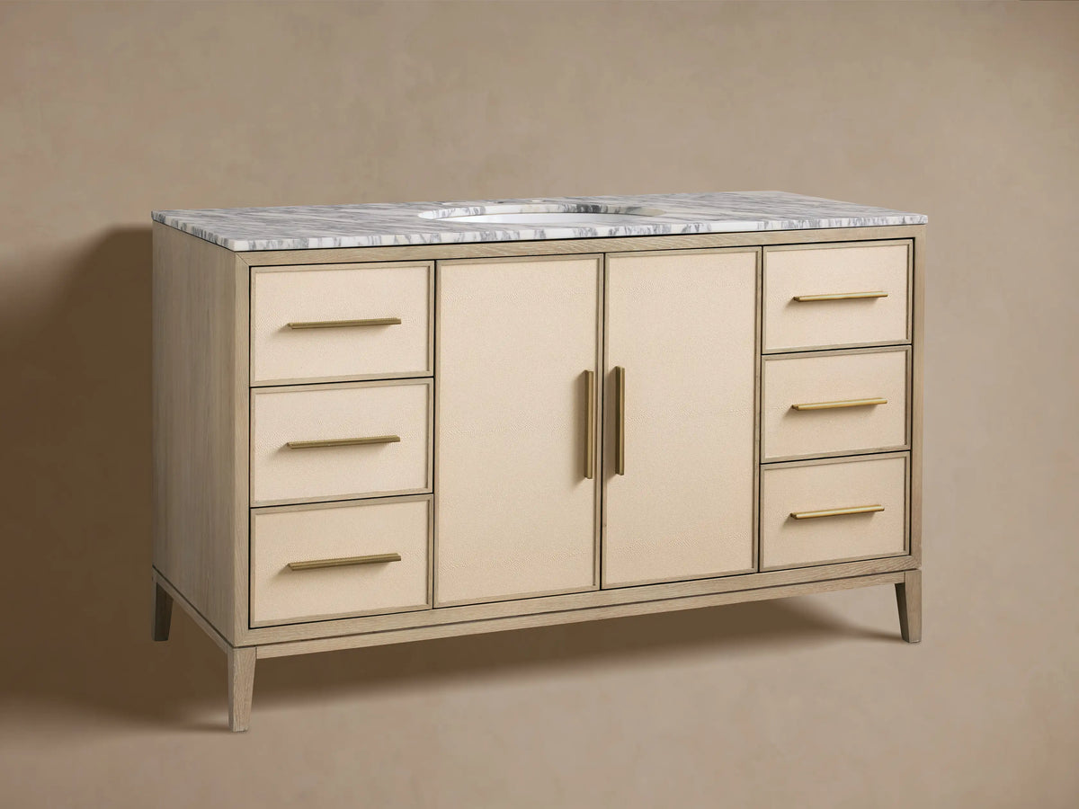 Malone Wide Single Vanity in bone finish oak with a white marble top, brass faucet, sink, and light beige shagreen doors/drawers.