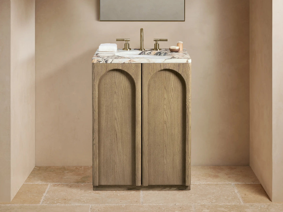 Provo Powder Vanity with oak wood finish, honed marble top, brass faucet, oval undermount sink, two arched doors, set against a neutral-toned bathroom.