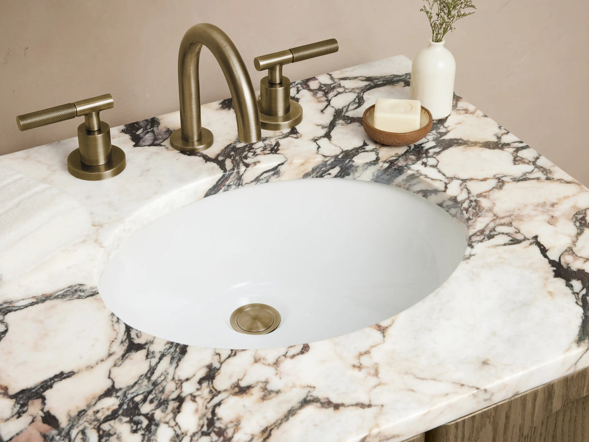 Provo Powder Vanity with oak wood finish, arched doors, marble stone top, brass faucet, on beige tiled floor.