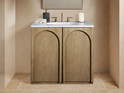 Provo Single Vanity: Light oak wood with visible grain, arched doors, white marble top, oval sink, and brass faucet in a modern setting.