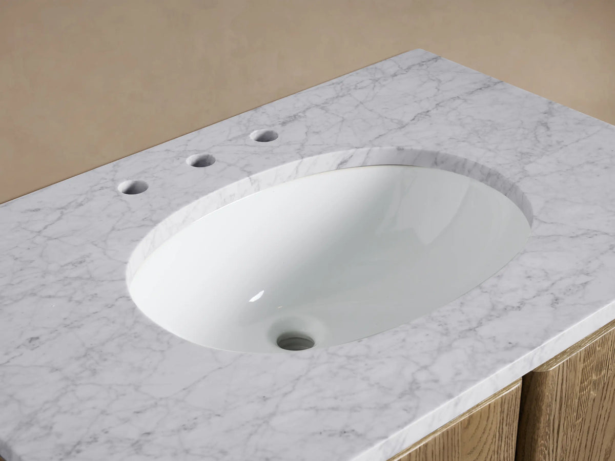 Provo Single Vanity with white oval sink, veined marble top, brass faucet, bar soap, cream towel, and wood grain cabinet.