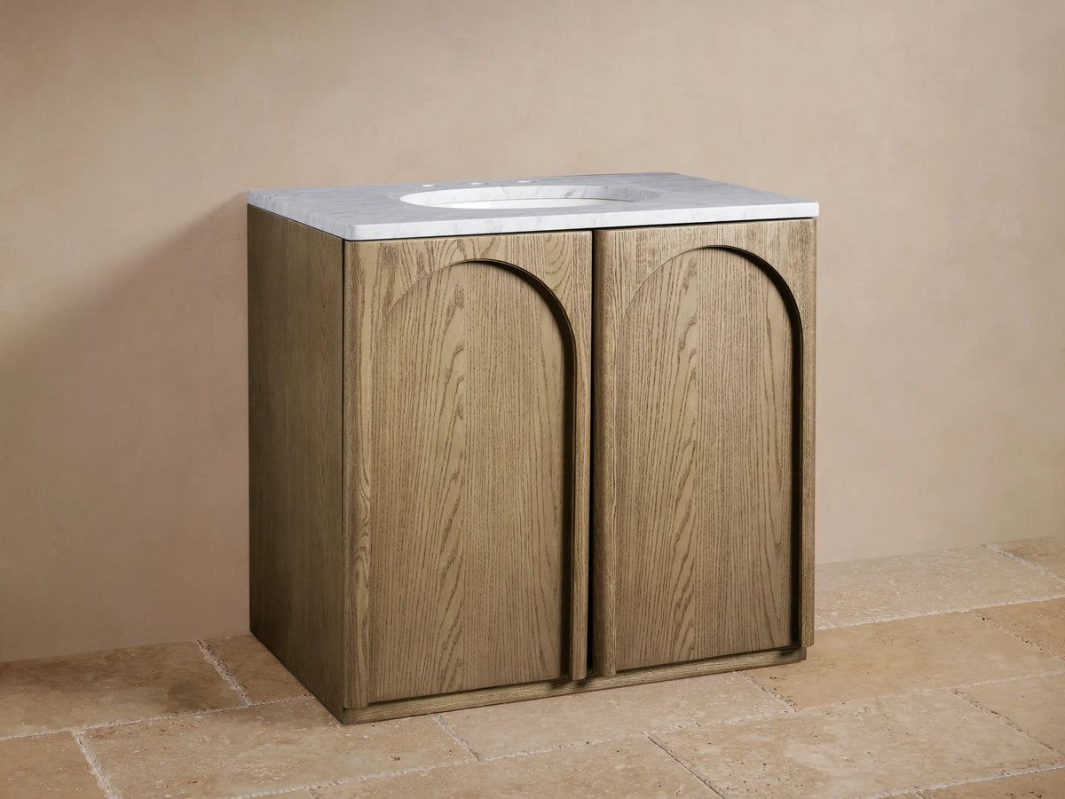 Provo Single Vanity: light oak wood vanity with arched doors, white marble top, oval sink, and brass faucet, on tiled floor.