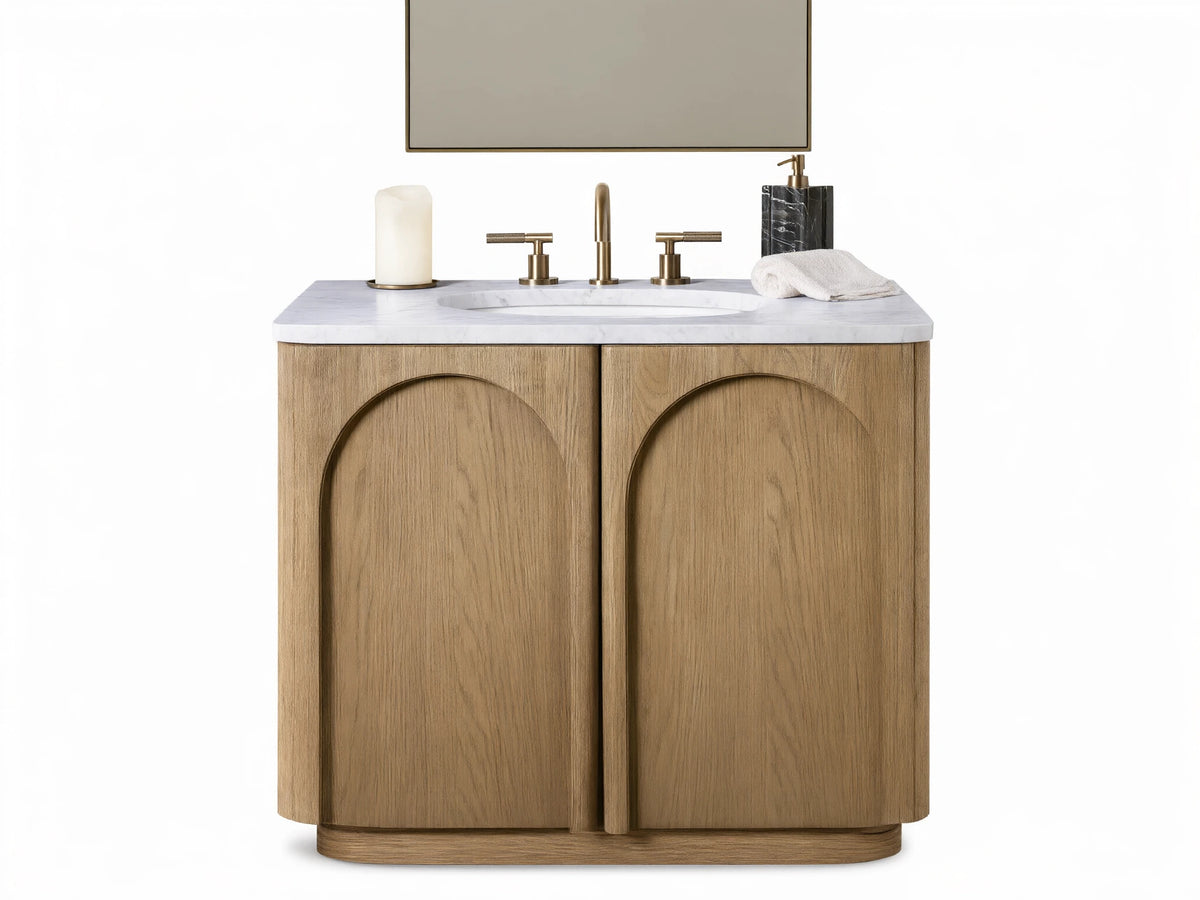 Provo Single Vanity: Light oak wood with visible grain, arched doors, white marble top, oval sink, and brass faucet in a modern setting.