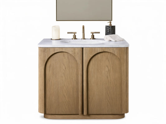 Provo Single Vanity: Light oak wood with visible grain, arched doors, white marble top, oval sink, and brass faucet in a modern setting.