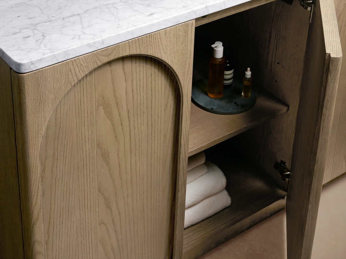 Oval ceramic sink with Carrara marble top featuring natural veining, bronze faucet, and decor items on Provo Single Wide Vanity.