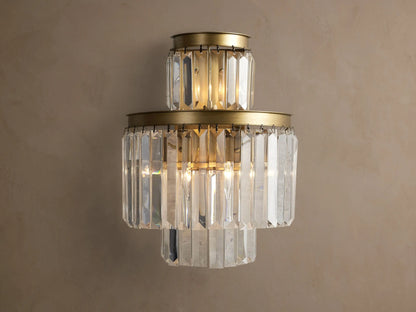 Leyland Sconce: a tiered wall light with illuminated clear K9 glass crystals & an oil-rubbed bronze-toned frame against a wall.