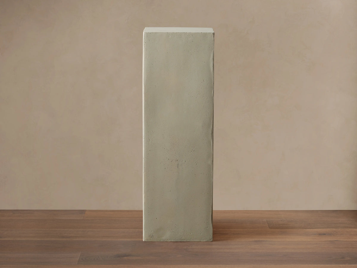 Light gray rectangular fiberglass Outdoor Pedestal standing on a dark wood floor against a beige wall.