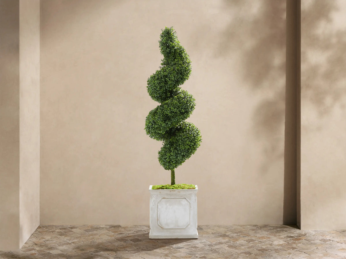 Boxwood Spiral Topiary, a tall green faux plant with a spiral shape, in a light gray square planter. Beige wall & stone floor.