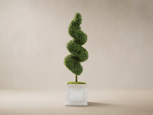 Boxwood Spiral Topiary, a tall green faux plant with a spiral shape, in a light gray square planter. Beige wall & stone floor.