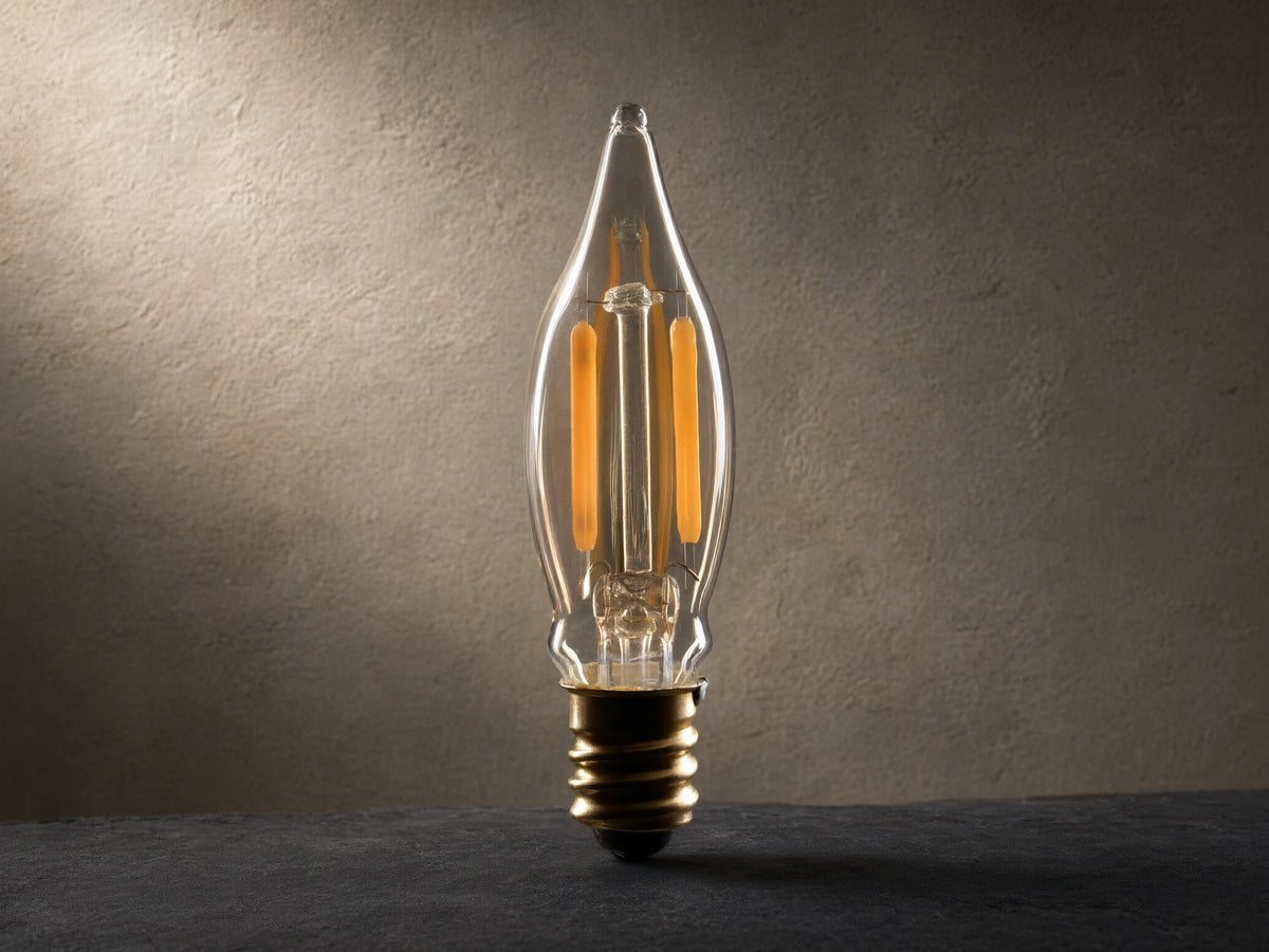 Front view of an LED Mini Filament E12 Bulb with amber glass, C18 shape, brass E12 base, and two vertical glowing orange filaments.