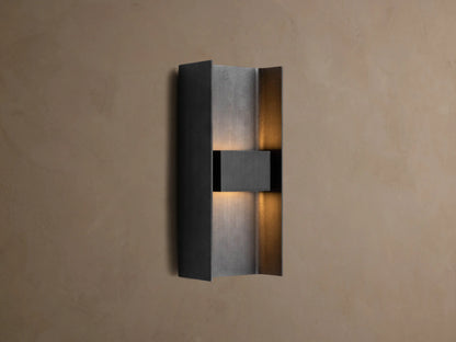 Sidney Outdoor Sconce, a graphite aluminum fixture casting warm LED light up and down against a taupe wall.