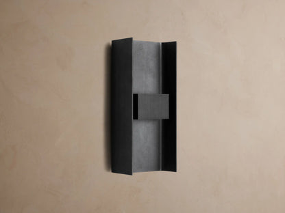 Sidney Outdoor Sconce, a graphite aluminum fixture casting warm LED light up and down against a taupe wall.