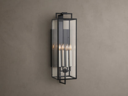 Hendricks Outdoor Sconce: black iron frame with clear glass panels, four lit candle-style bulbs, mounted vertically on a taupe wall.