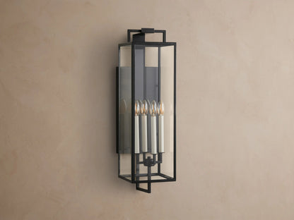 Hendricks Outdoor Sconce: black iron frame with clear glass panels, four lit candle-style bulbs, mounted vertically on a taupe wall.