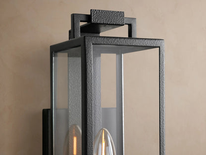 Hendricks Outdoor Sconce, black hand-worked iron and clear glass, rectangular, with one candelabra bulb, on a tan wall.