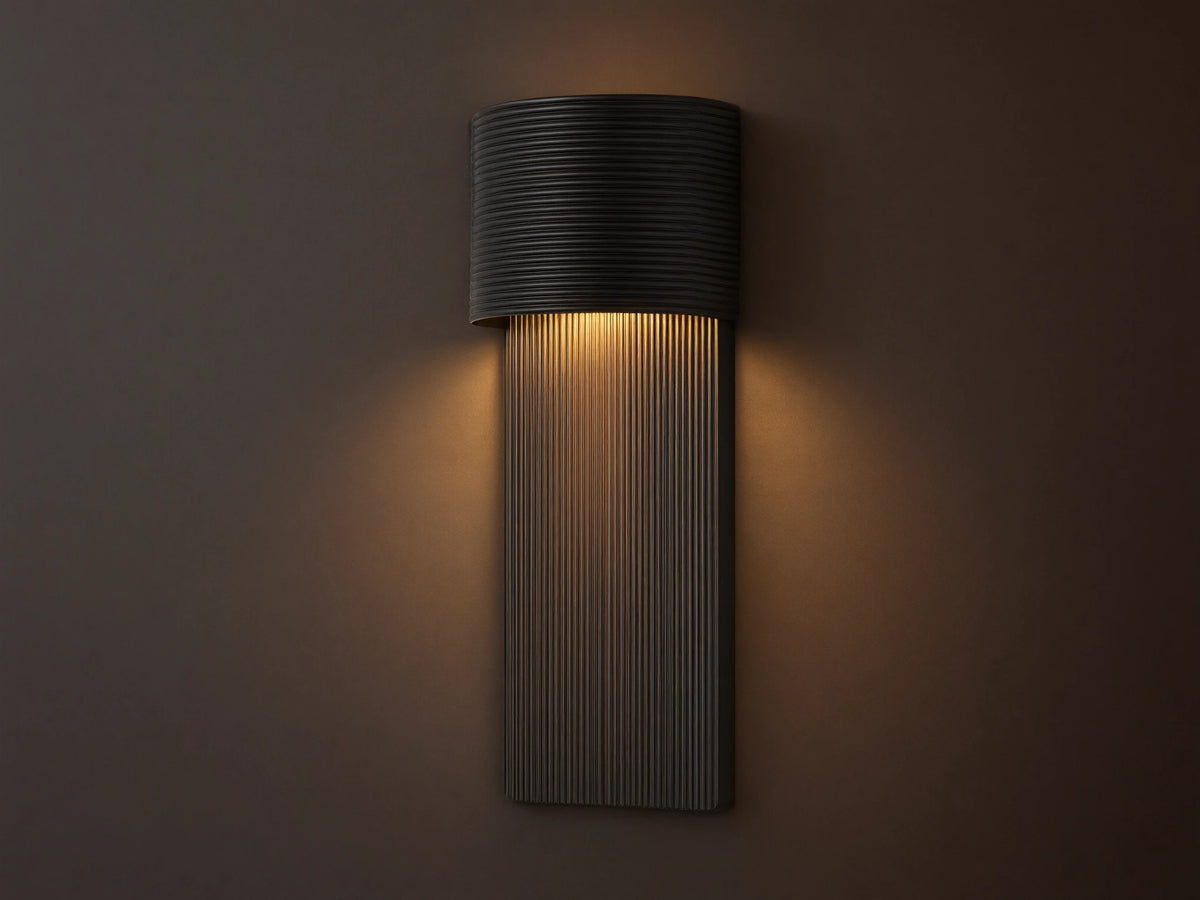 Fultz Outdoor Sconce, a soft black wall-mounted fixture with a horizontally ridged top and vertically ridged base, glowing warm light.