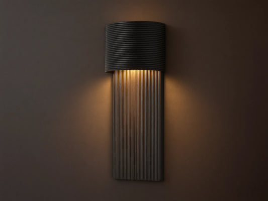 Fultz Outdoor Sconce, a soft black wall-mounted fixture with a horizontally ridged top and vertically ridged base, glowing warm light.
