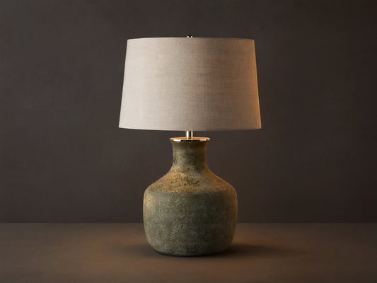Galena Table Lamp: Green, sand-blasted glass bottle-shaped base with a light linen shade on a rustic wood surface.