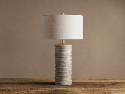 Maeve Taupe Table Lamp with a distressed stacked taupe cylindrical base & a light beige fabric drum shade.