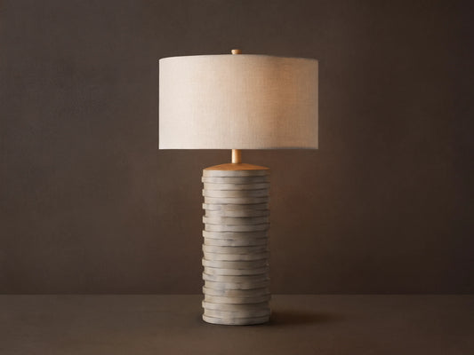 Maeve Taupe Table Lamp with a distressed stacked taupe cylindrical base & a light beige fabric drum shade.