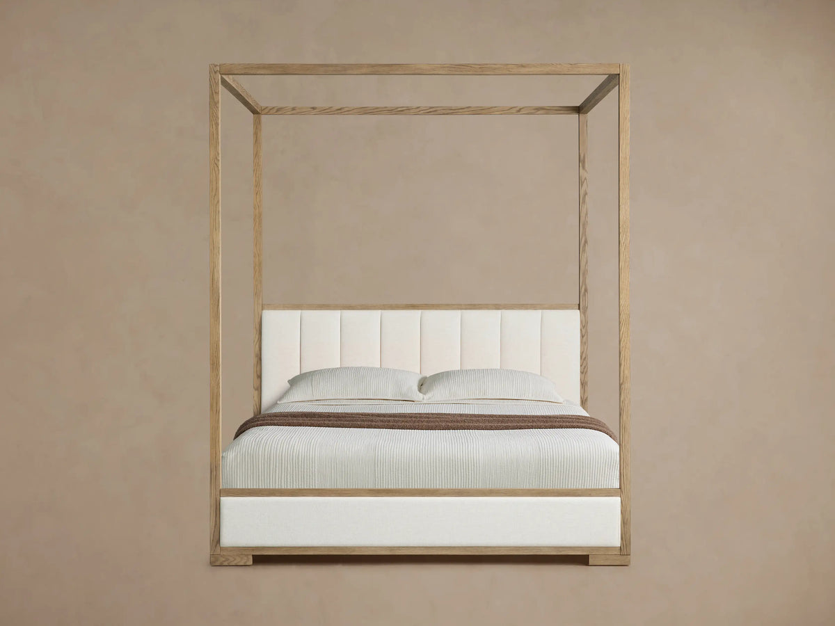 Darien Channel-Stitched Canopy Bed. Light oak frame, white channel-stitched headboard & base, light beige bedding with brown throw.