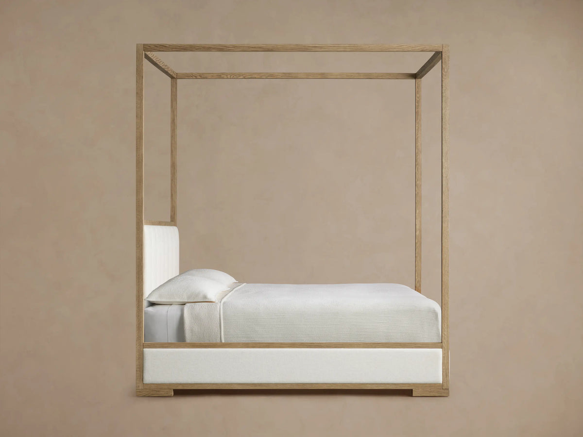 Close-up of Darien Channel-Stitched Canopy Bed, showing light oak wood frame and off-white channel-stitched upholstered headboard.