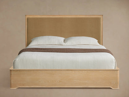 Light oak Conley Panel Bed with tan fabric headboard, white bedding, and brown throw, angled on a wooden floor.