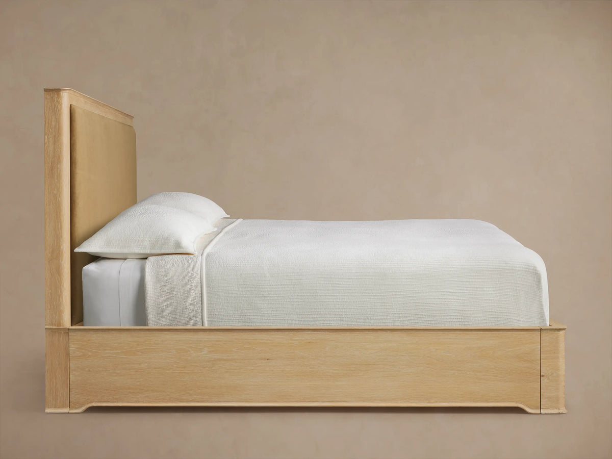 Conley Panel Bed headboard close-up. Light oak wood frame with rounded left corner and a gold-tan upholstered panel.