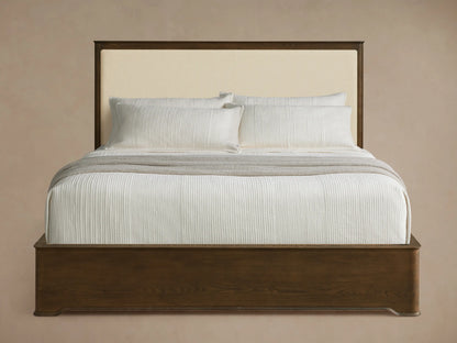 Conley Panel Bed with dark oak frame & cream upholstered headboard. Bed has white textured bedding & a gray throw blanket.