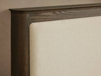 Conley Panel Bed: Dark oak wood frame with a cream upholstered headboard, white quilted bedding, and a grey throw.