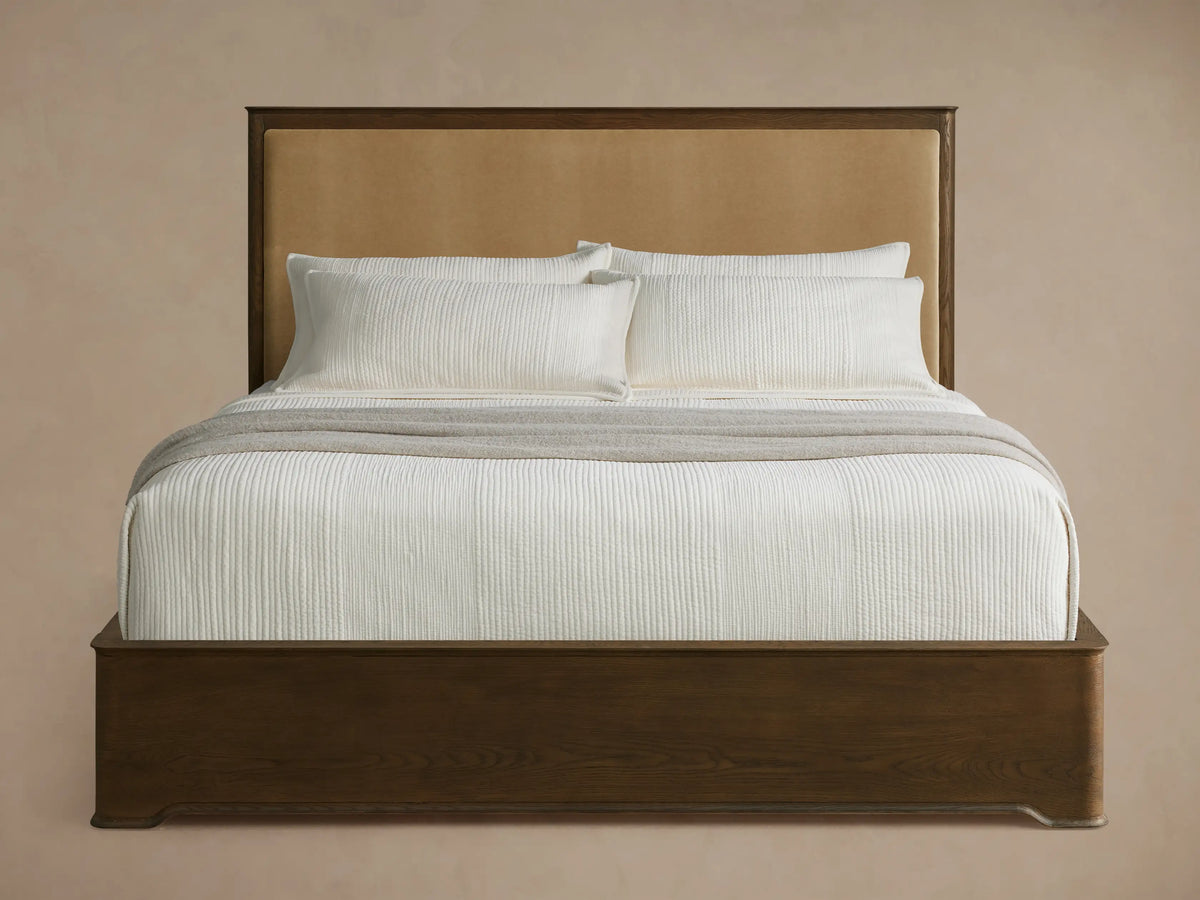 Conley Panel Bed with dark wood frame, tan upholstered headboard, white textured bedding, and gray throw in a bright room.