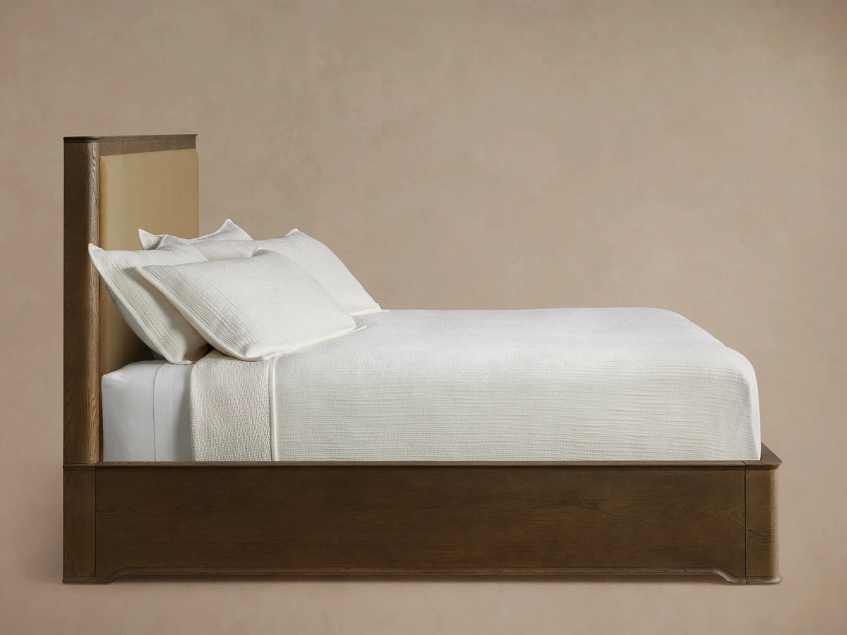 Conley Panel Bed headboard close-up showing a dark oak wood frame with visible grain and a light brown fabric panel.