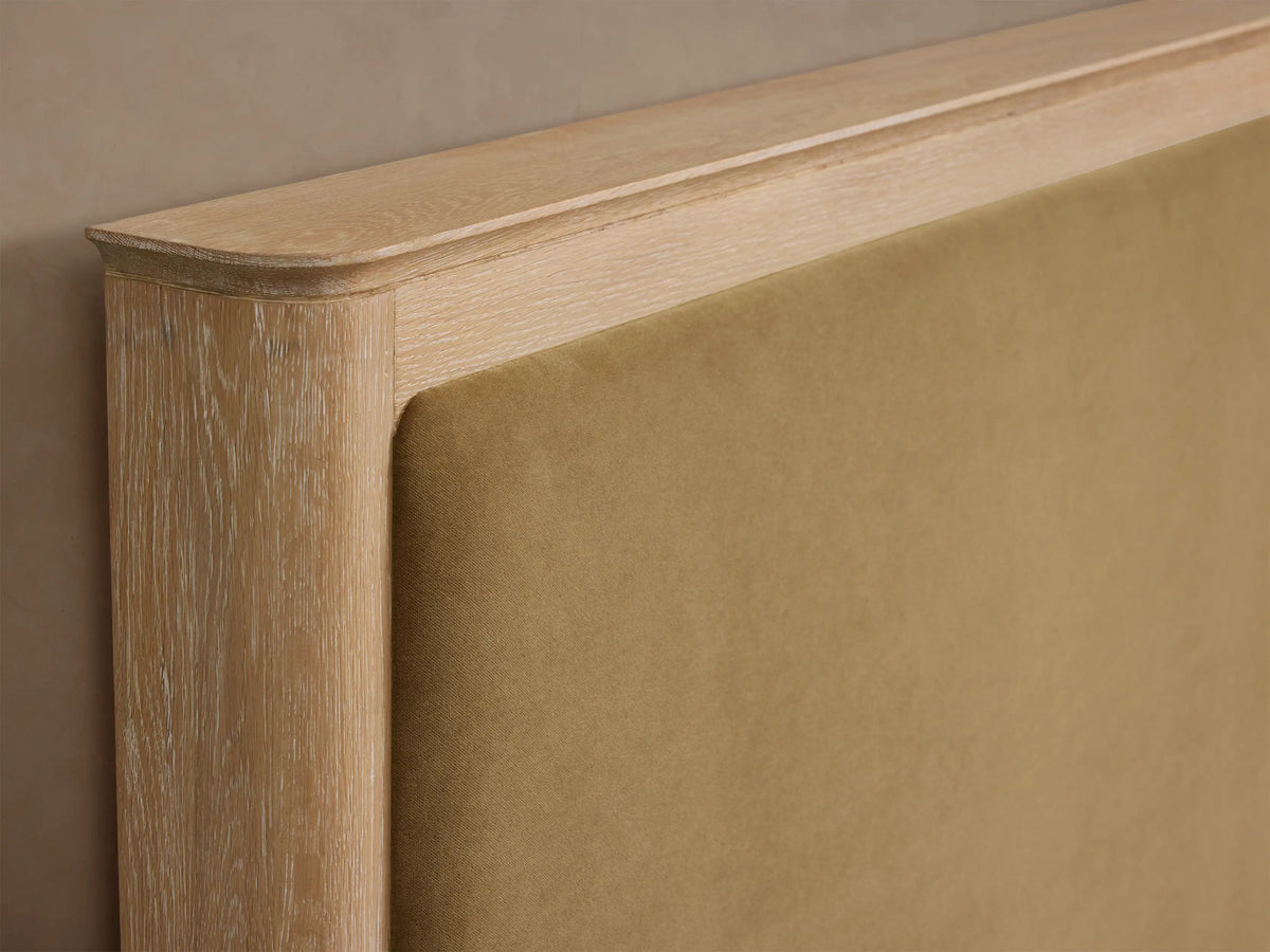 Conley Panel Bed: light oak wood frame, tan fabric upholstered headboard, white textured bedding, and brown throw blanket.