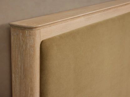 Conley Panel Bed: light oak wood frame, tan fabric upholstered headboard, white textured bedding, and brown throw blanket.