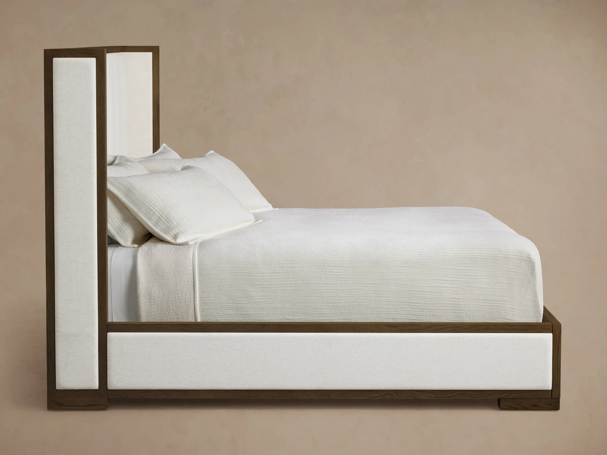 Close-up of the dark brown oak frame and off-white upholstered panels of the Darien Channel-Stitched Shelter Bed.