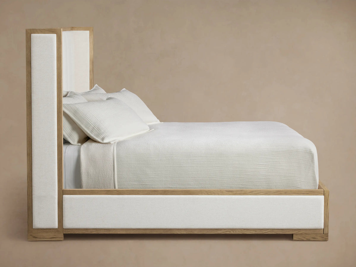 Close-up of Darien Shelter Bed corner, showing light oak wood frame with visible grain and cream channel-stitched upholstery.
