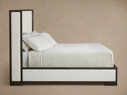 Close-up of Darien Channel-Stitched Shelter Bed's dark wood frame corner, featuring beige upholstered side & white channel-stitched headboard.