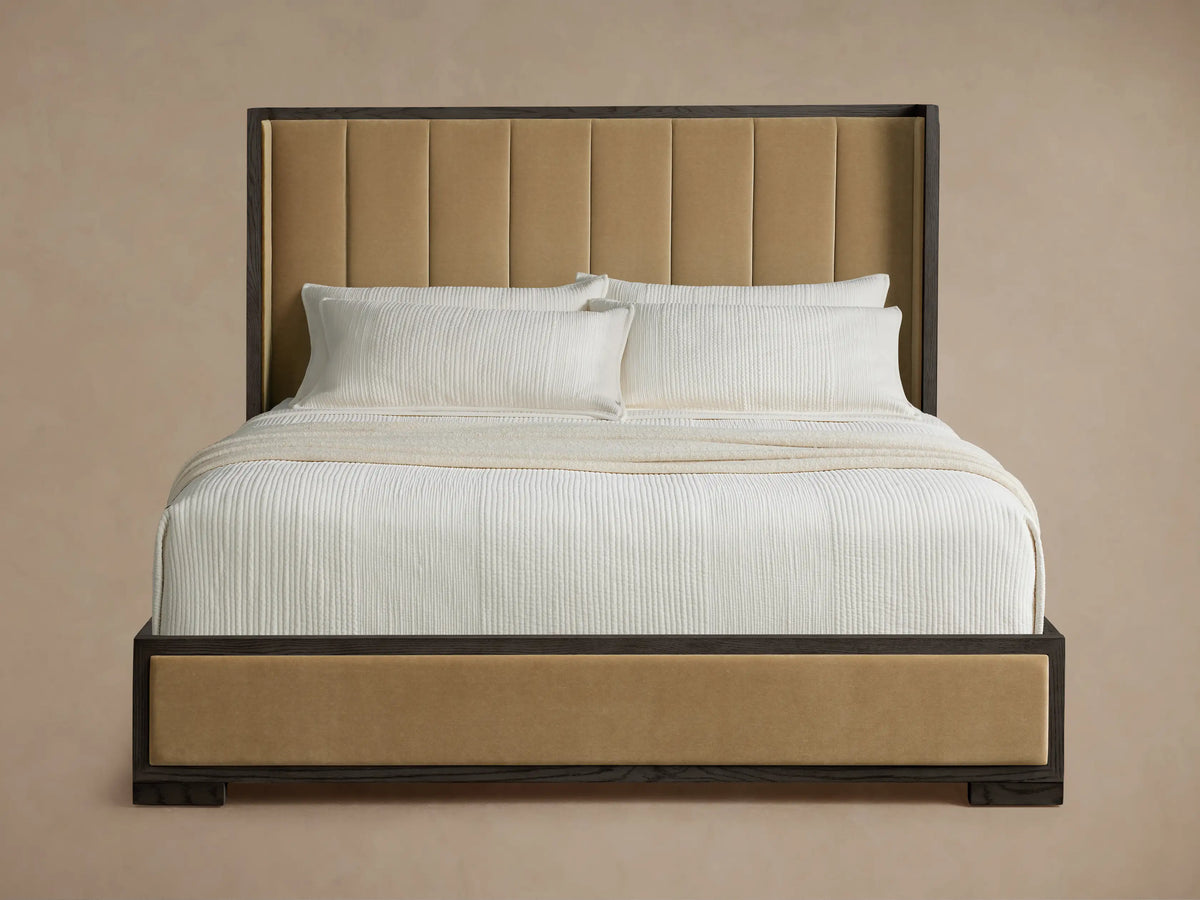 Tan channel-stitched Darien Shelter Bed with dark wood frame, angled view. Features white ribbed bedding & pillows on light wood floor.