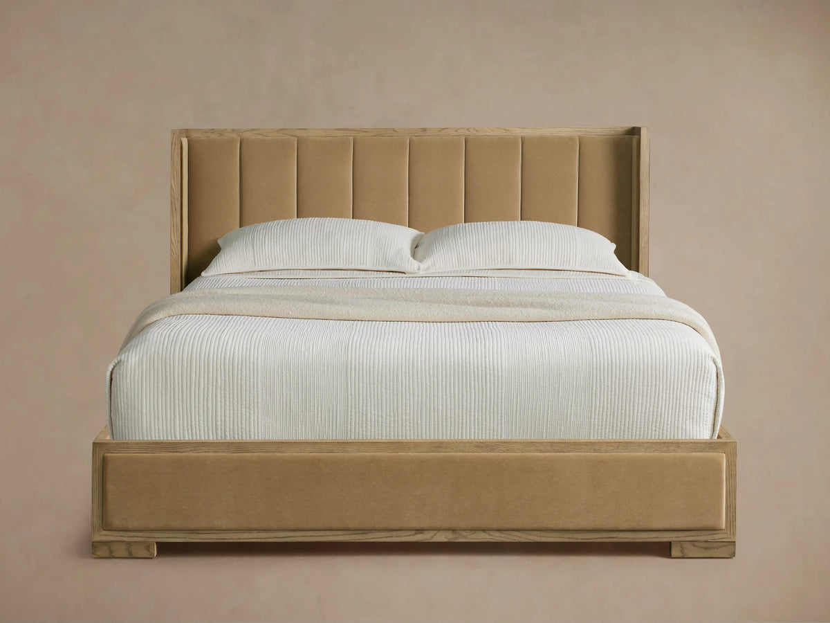 Darien Channel-Stitched Shelter Bed with tan upholstered headboard & footboard, light oak frame, white textured bedding on wood floor.
