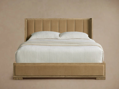 Darien Channel-Stitched Shelter Bed with tan upholstered headboard & footboard, light oak frame, white textured bedding on wood floor.