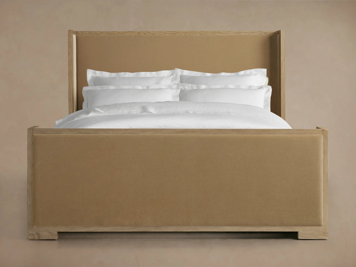 Darien Shelter Bed with oak frame, beige upholstered high footboard, and white bedding, against a neutral background.
