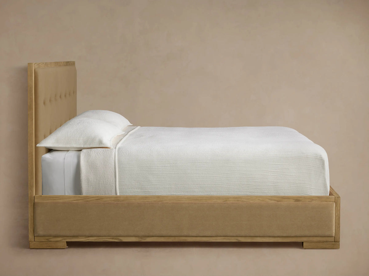 Close-up of Darien Box-Tufted Panel Bed headboard. Light oak wood frame with visible grain, surrounding beige box-tufted fabric.