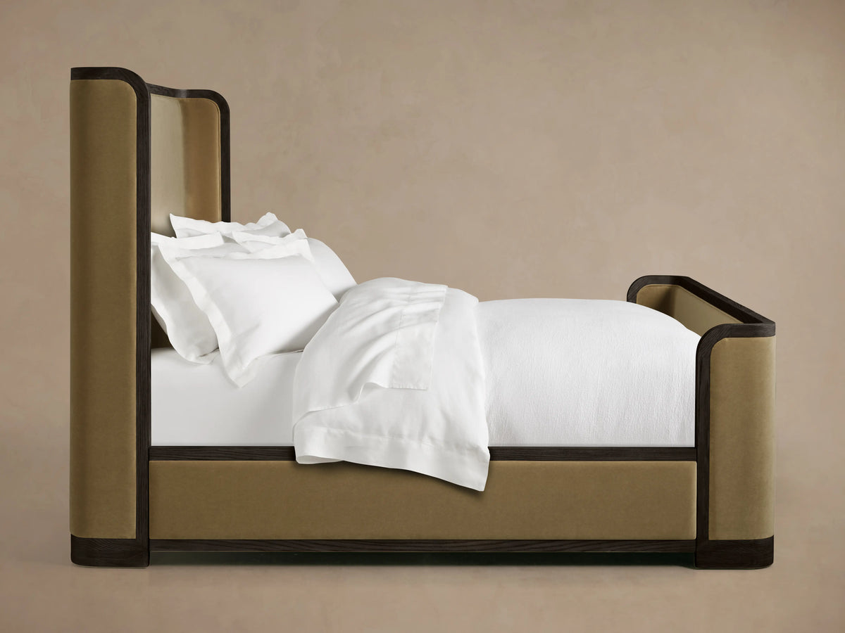 Darien Curved Shelter Bed in oak wood with high footboard, upholstered panels, white bedding, and pillows, side view.