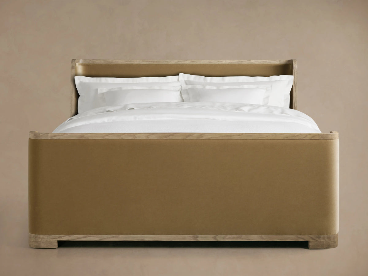 Darien Curved Shelter Bed in oak with high footboard, beige upholstered panels, white bedding, on wooden floor, side view.